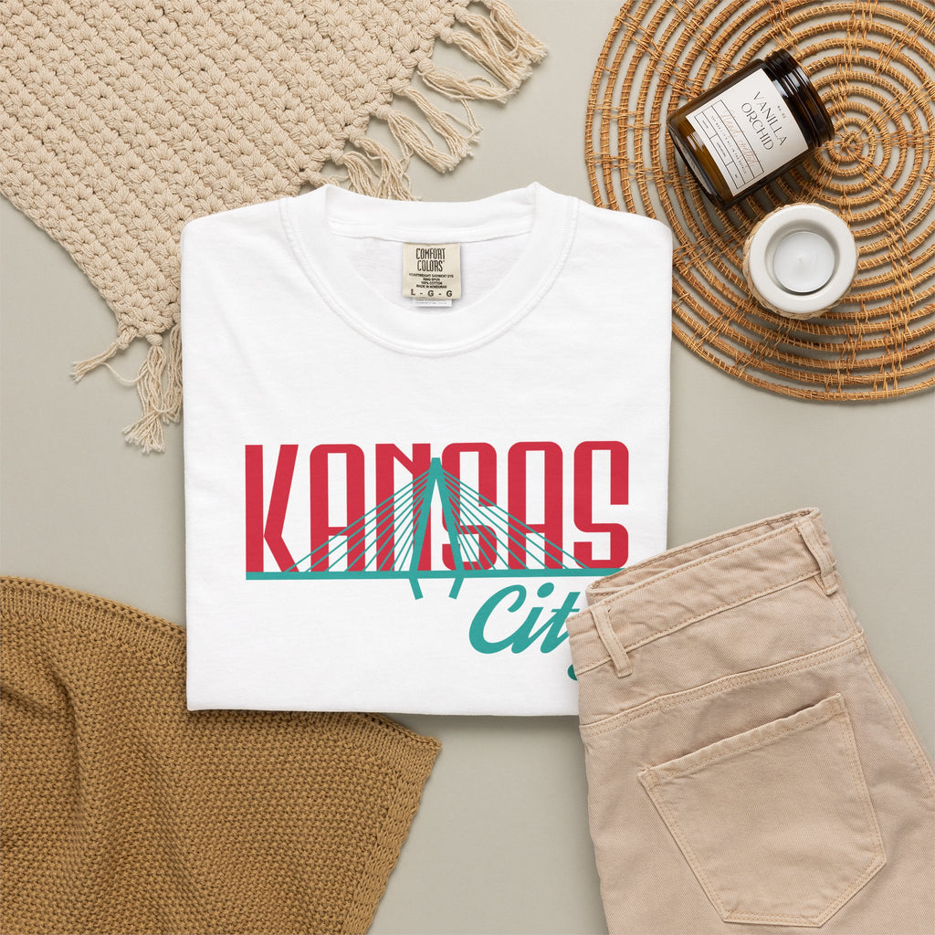 White garment-dyed t-shirt front view featuring "Kansas City" with bridge graphic in red and teal retro script across the chest.