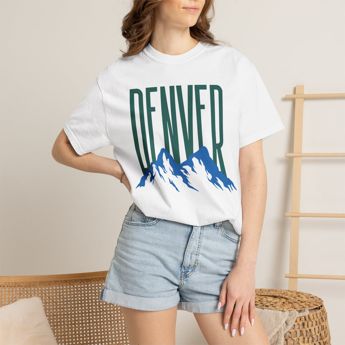 White Denver mountain graphic t-shirt featuring block lettering above a blue Rocky Mountain silhouette, ideal for game day fan gear.