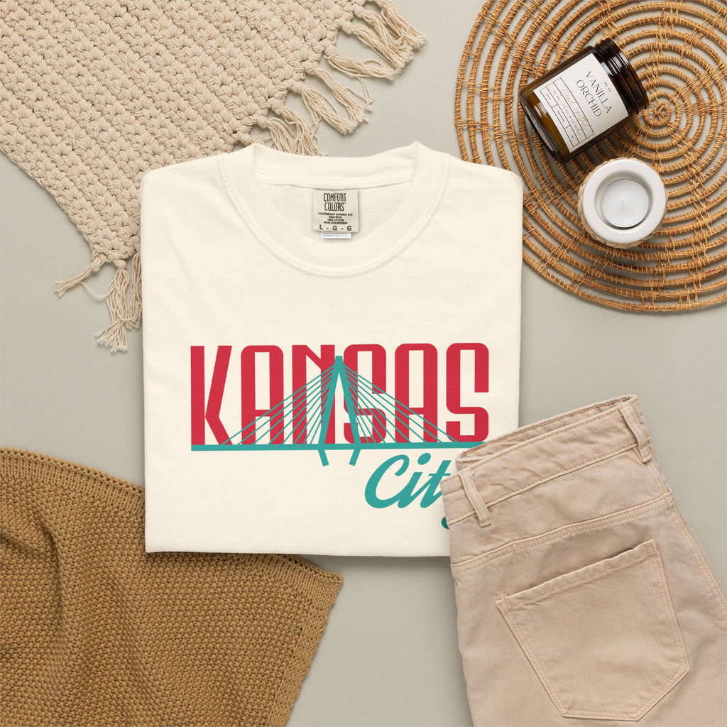 Ivory garment-dyed t-shirt front view featuring "Kansas City" with bridge graphic in red and teal retro script across the chest.