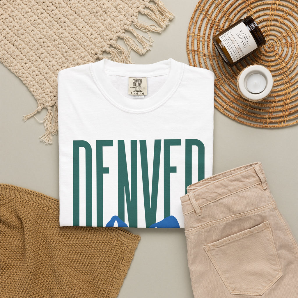 White Denver mountain graphic t-shirt featuring block lettering above a blue Rocky Mountain silhouette, ideal for game day fan gear.