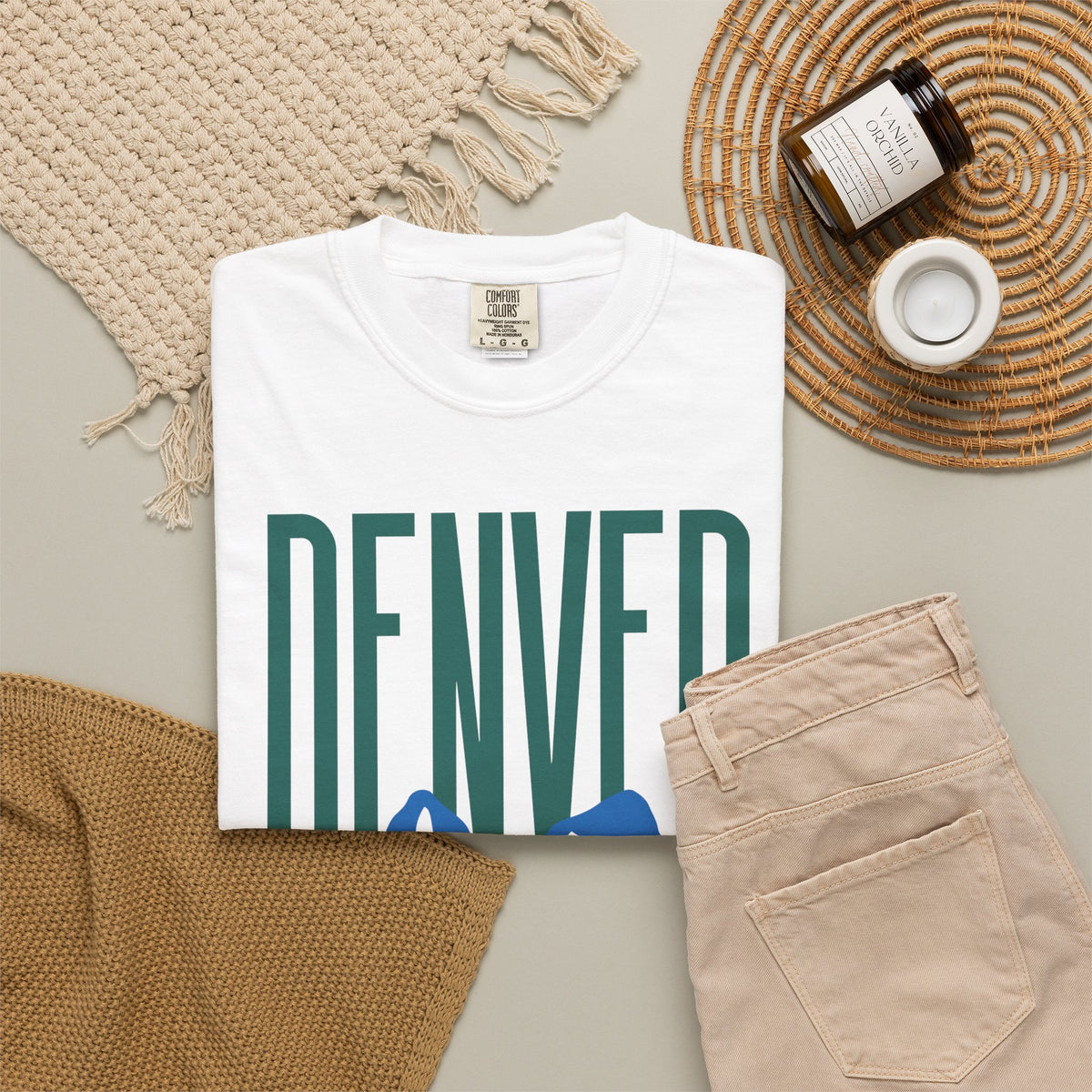 White Denver mountain graphic t-shirt featuring block lettering above a blue Rocky Mountain silhouette, ideal for game day fan gear.