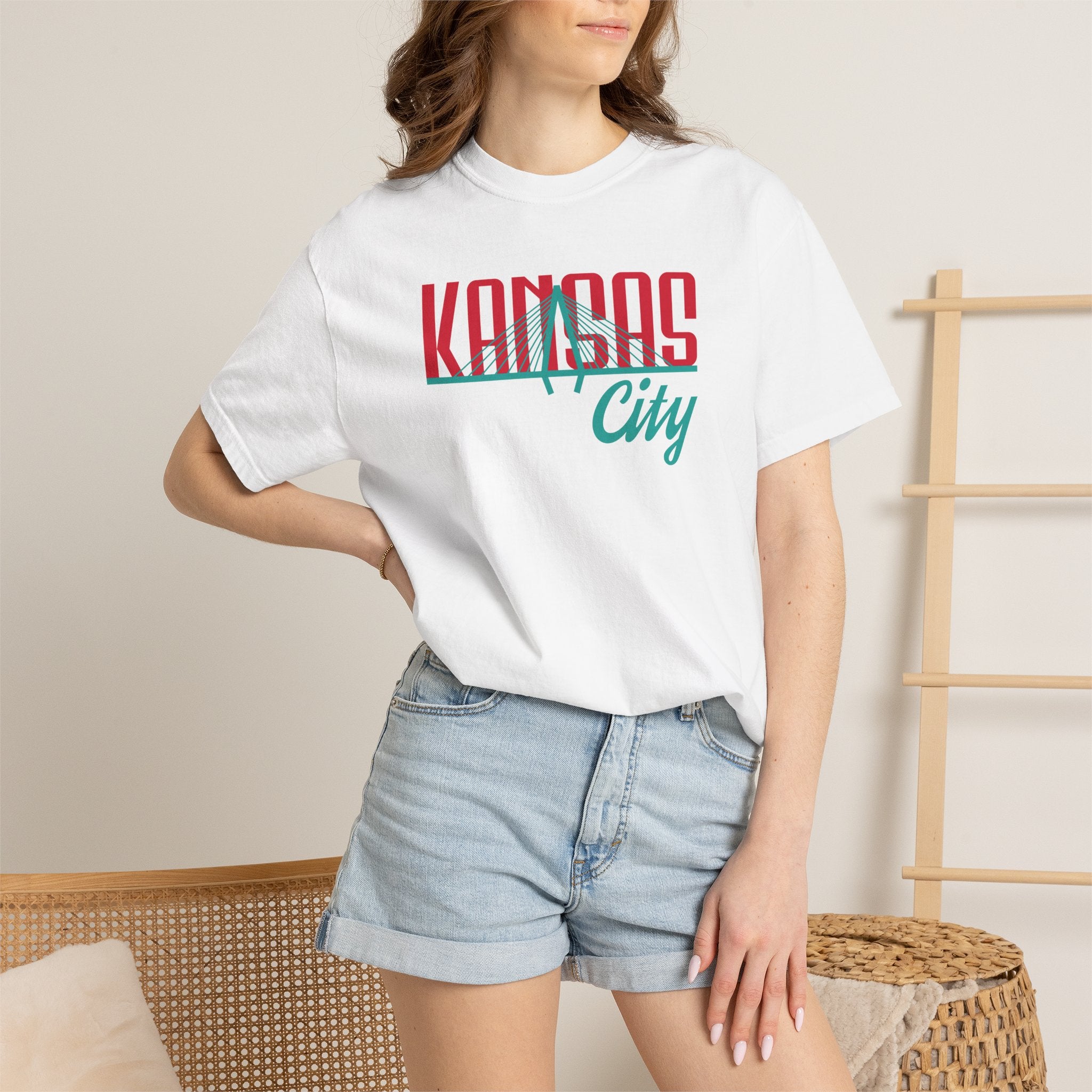 White garment-dyed t-shirt front view featuring "Kansas City" with bridge graphic in red and teal retro script across the chest.