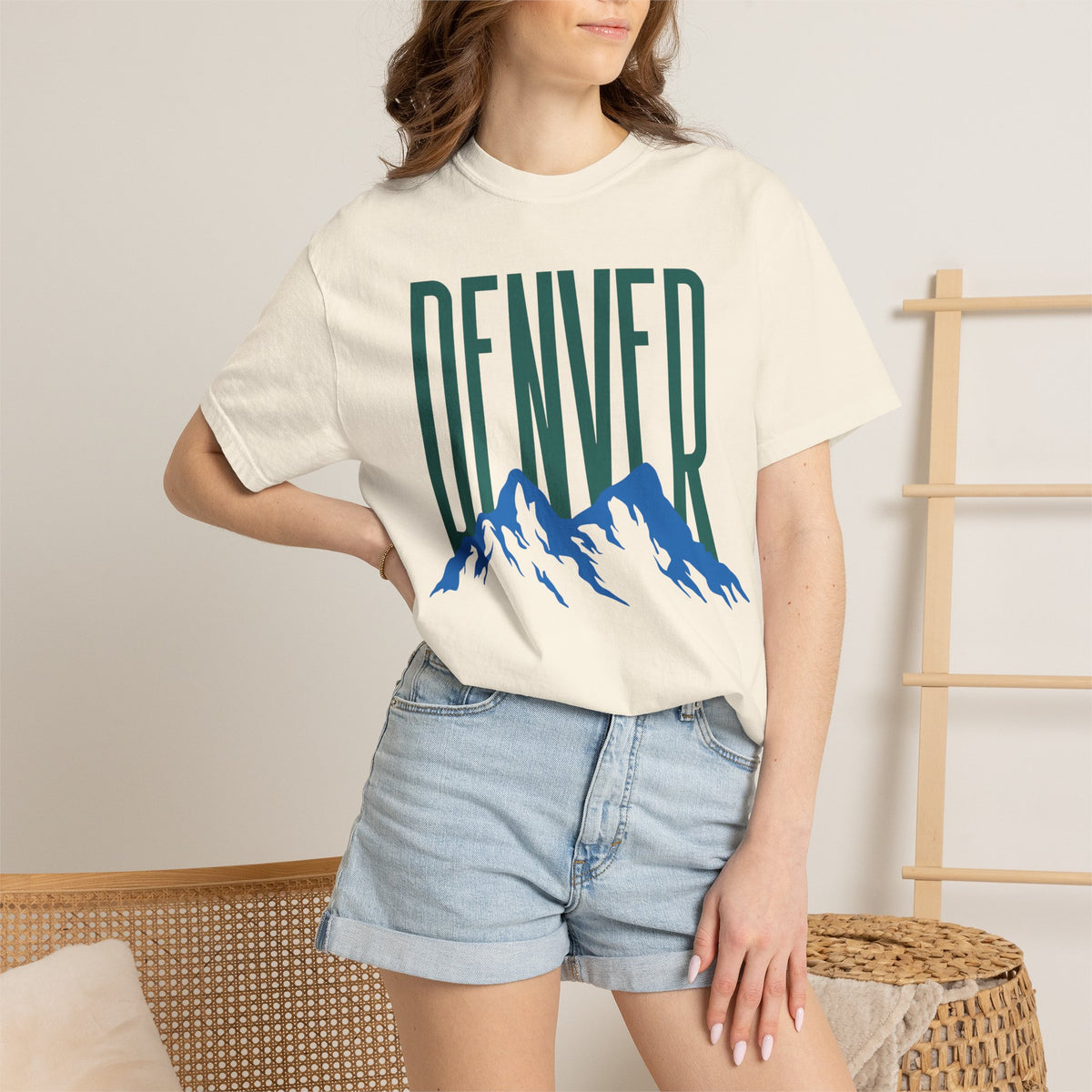 Ivory Denver mountain graphic t-shirt featuring block lettering above a blue Rocky Mountain silhouette, ideal for game day fan gear.